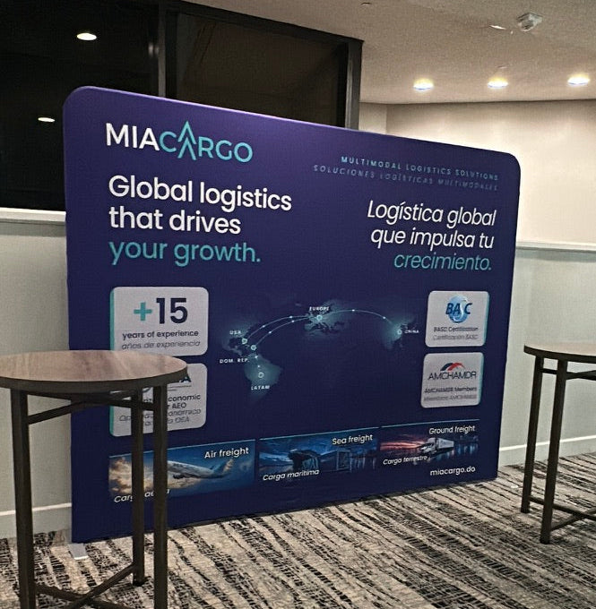 A large blue and white MIA CARCO promotional display board in a meeting room or office space, with carpeted floor and small tables visible.