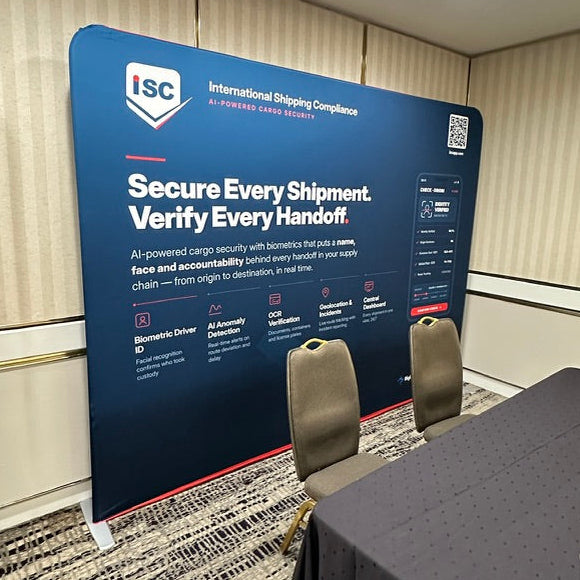 A large blue ISC International Shipping Compliance display board in a conference room, with chairs in front and a table covered in a dark cloth in the foreground.